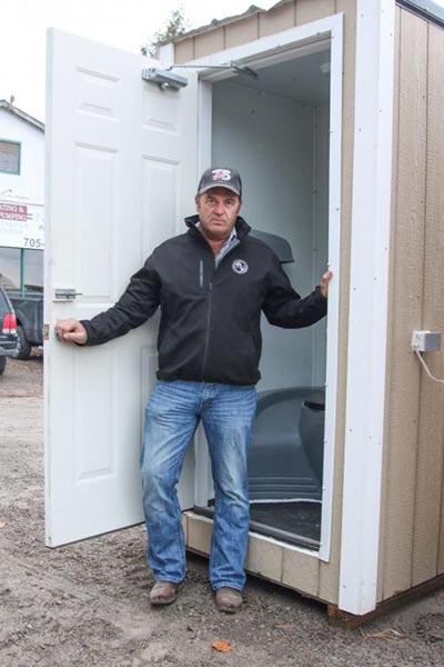 Mike Clark standing in the doorway of a custom-made, heated, outdoor flush toilet