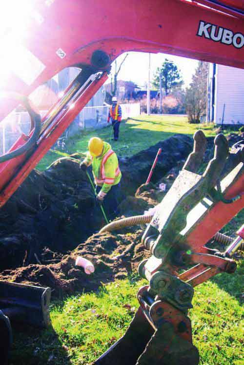 Mike Clark digs a trench for a septic installation while Billy Clark monitors the progress.